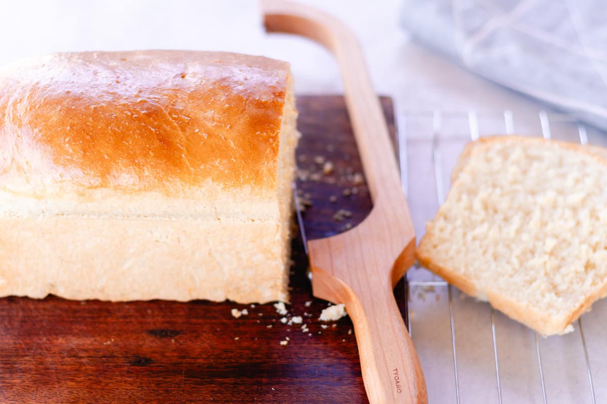 Half a loaf of bread on a cutting board with a bread knife.