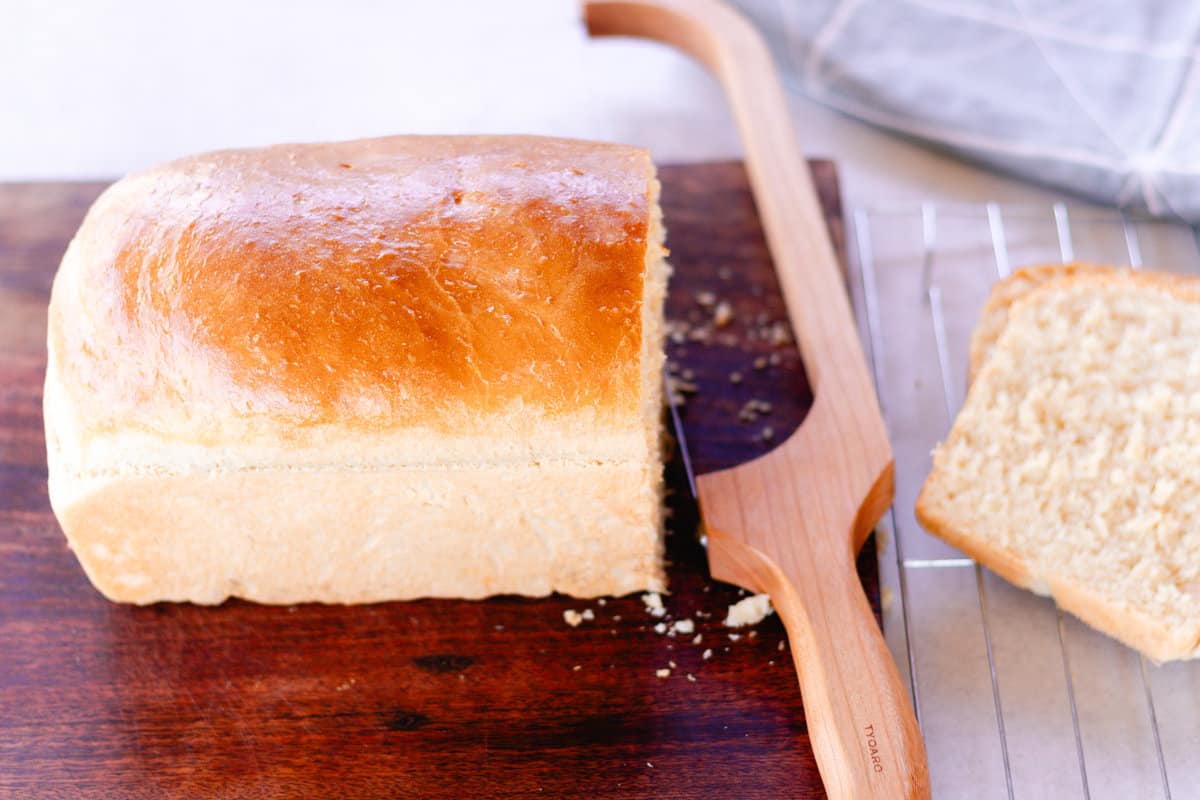 Slicing the loaf bread with a bread knife on a wooden cutting board. 