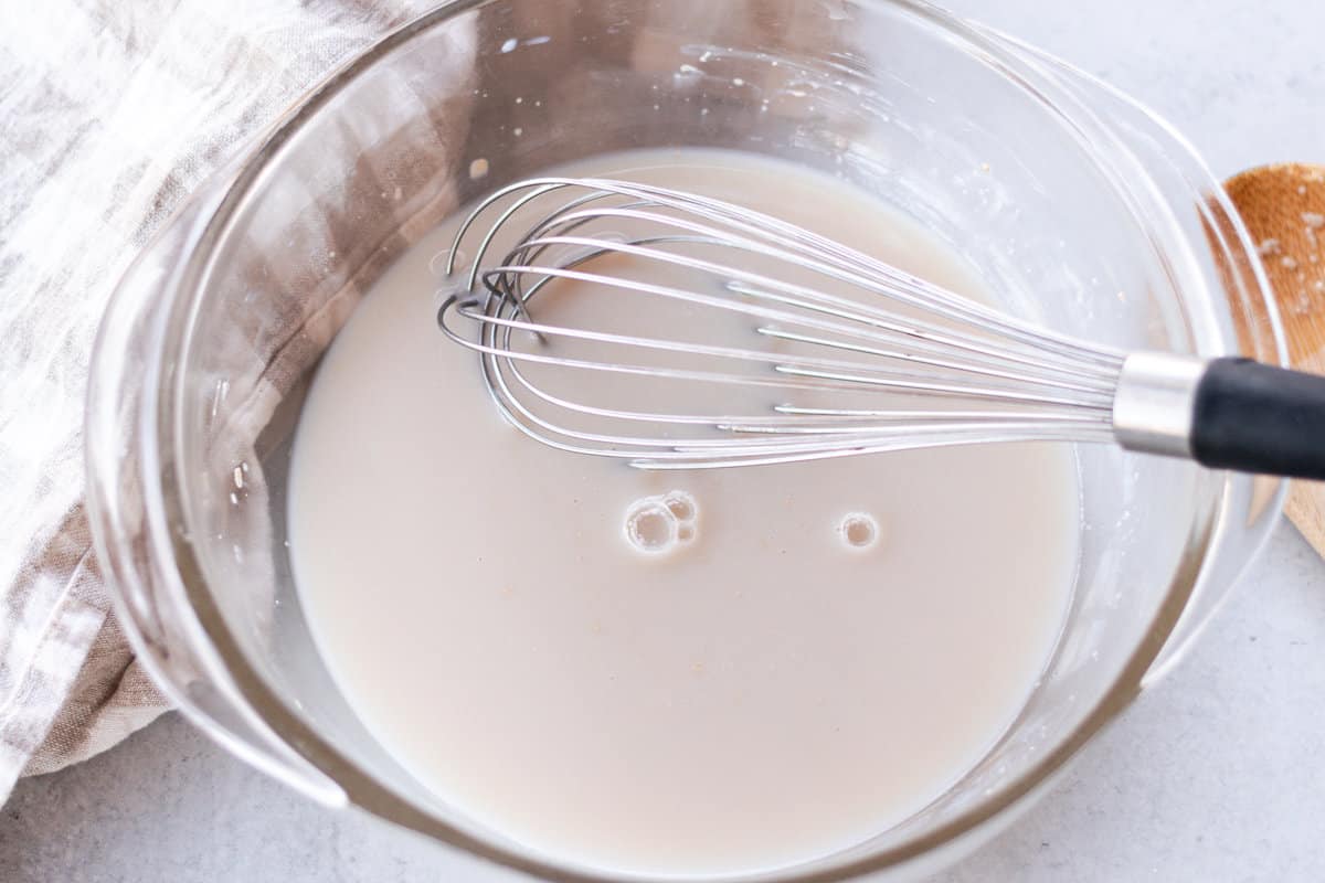 Whisking yeast, water and milk together in a glass bowl.