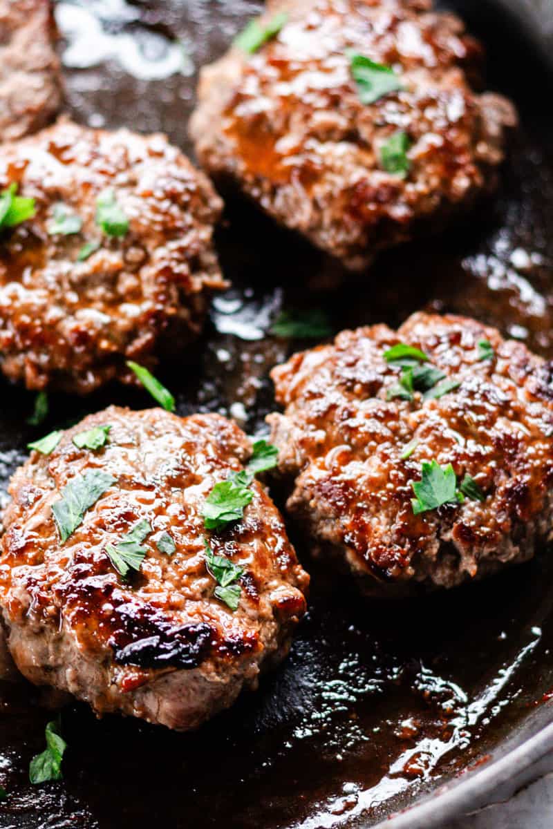 Perfectly seared moose patties with parsley on a large skillet.