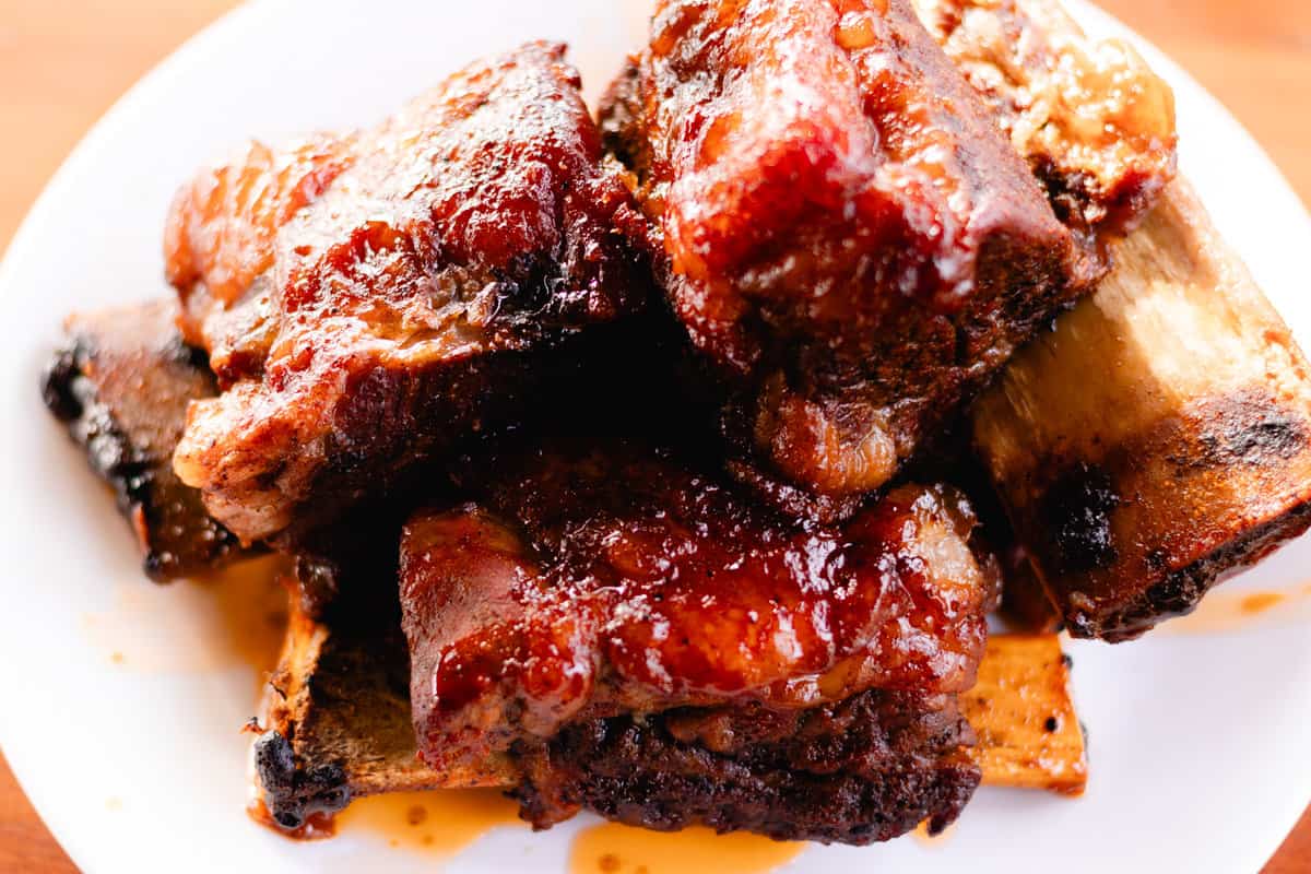 Juicy beef short ribs smothered with a creamy bbq sauce on a white plate.