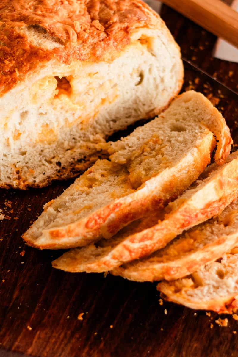 Dutch oven cheese bread sliced on a wooden cutting board.
