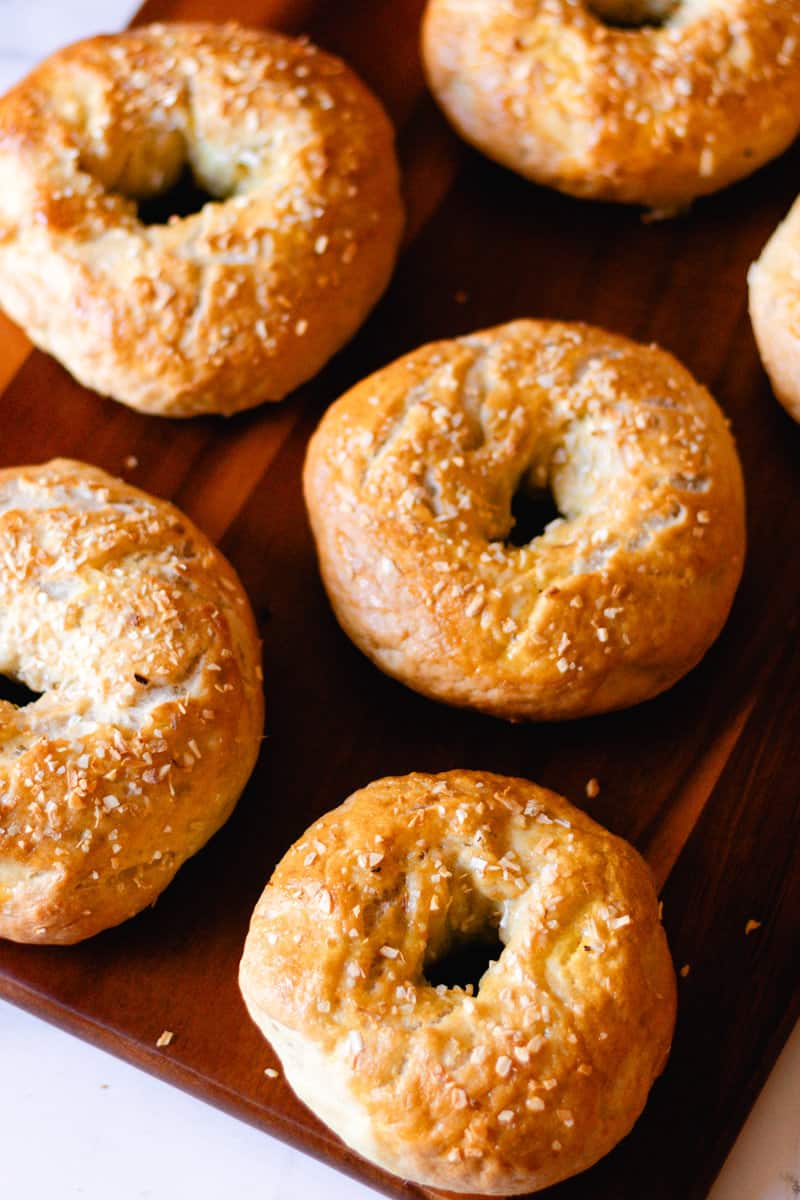 Homemade onion bagels cooling on a wooden tray on a marble countertop.