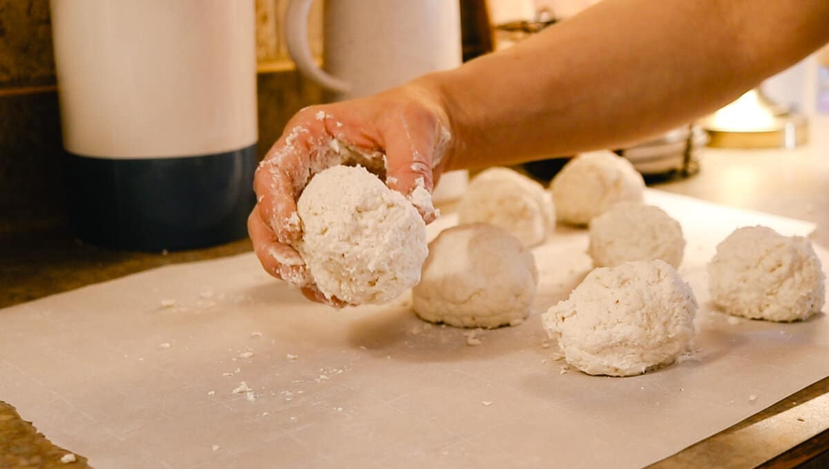 A woman placing raw bagel dough balls onto a sheet of parchment paper.