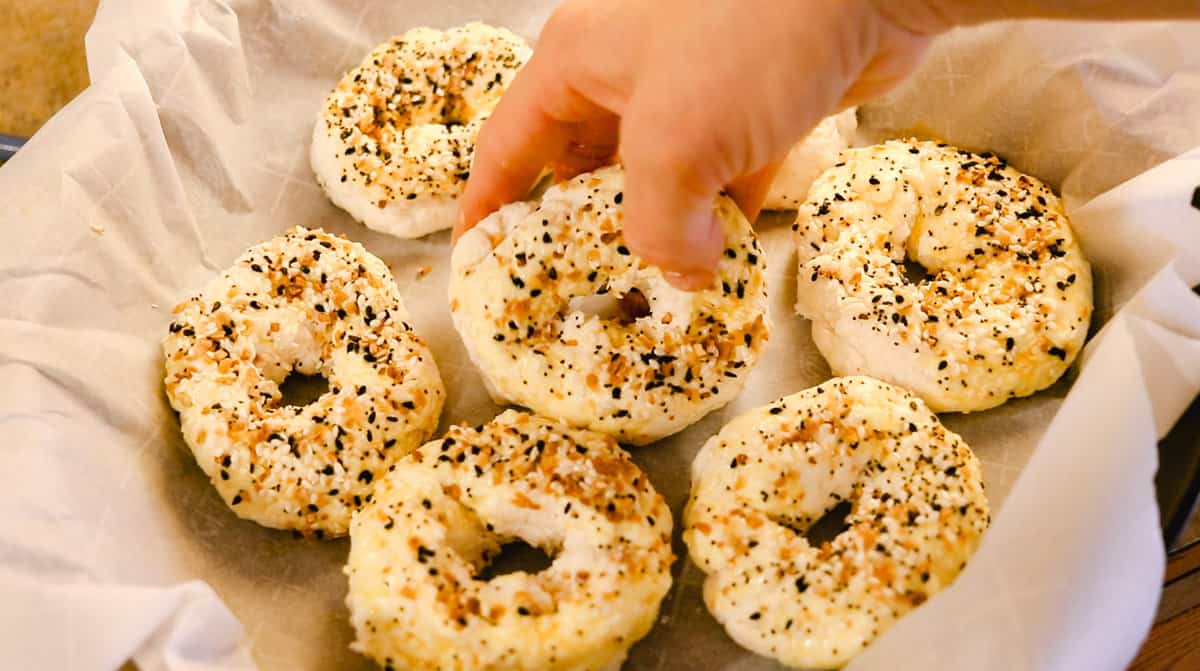 A woman's hand placing raw homemade bagels that are ready to be baked into a parchment-lined cast iron skillet.