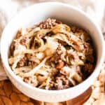 A bowl of cabbage and ground beef on a wooden table with a light colored tea towel next to it.