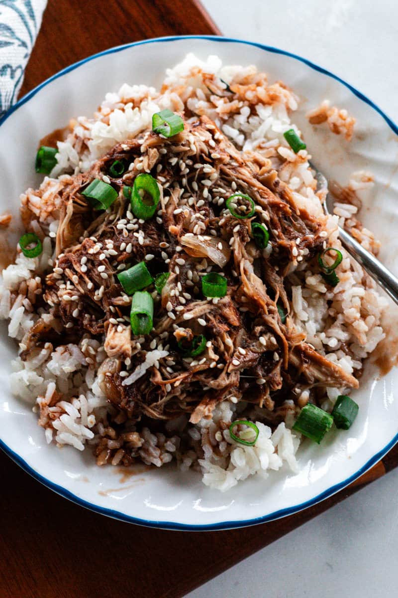 A plate of sweet and spicy shredded chicken garnished with green onions and toasted sesame seeds.