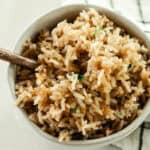 Scooping rice pilaf out of a bowl with a golden fork.