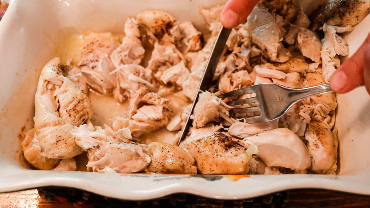 Chopping the cooked chicken up with a knife and fork.