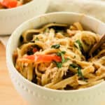 Bowl full of cajun chicken pasta with sautéed vegetables on a wooden table.