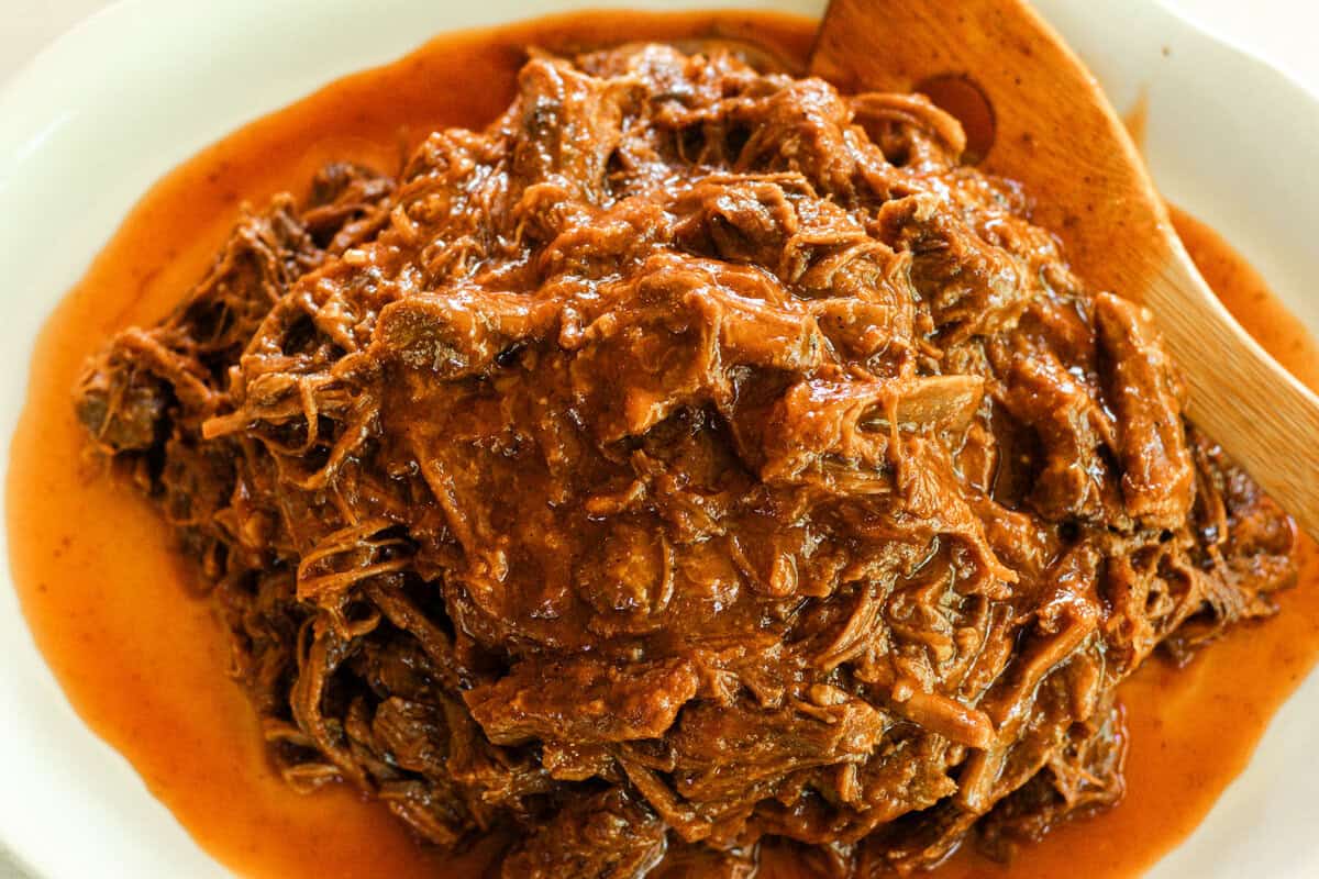 Pulled bbq beef on a plate after it has simmered on the stove.