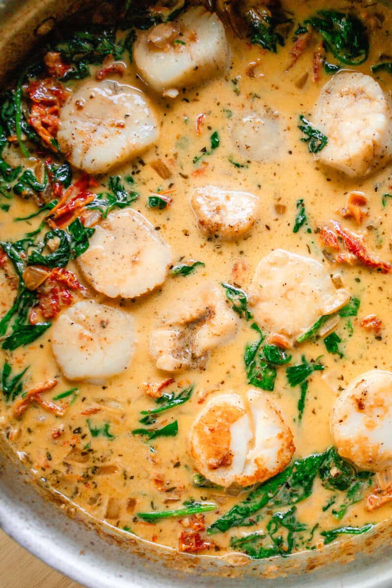 Tuscan scallops with a cream sauce and sun dried tomatoes being served out of a large frying pan. 