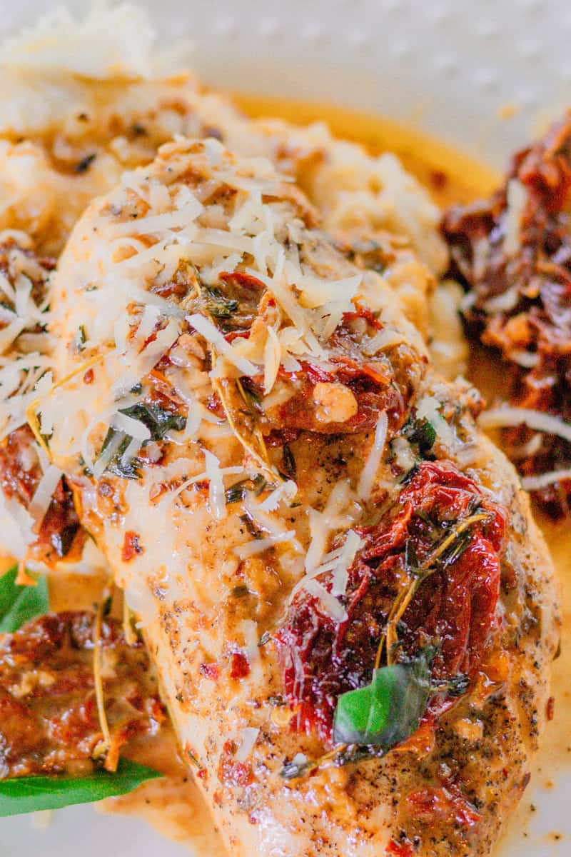 Chicken breast with cheese and sun dried tomatoes on a plate of creamy sauce with mashed potatoes underneath.