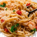Buttery garlic shrimp with pasta and cooked tomatoes on a white decorative plate.