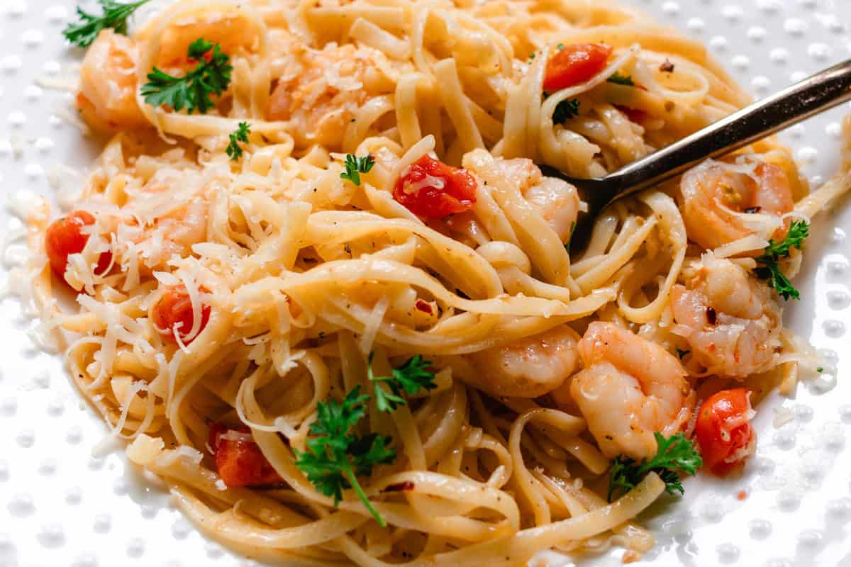 Buttery garlic shrimp with pasta and cooked tomatoes on a white decorative plate.