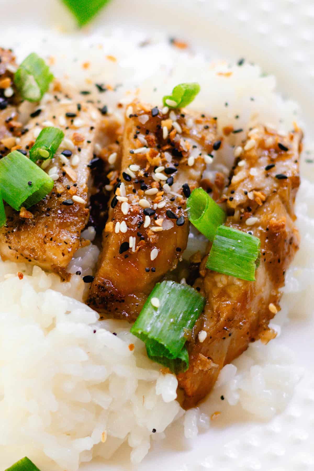 Sauce drips off the sides of the chicken as it is stacked on top of a bed of white rice on a white plate.