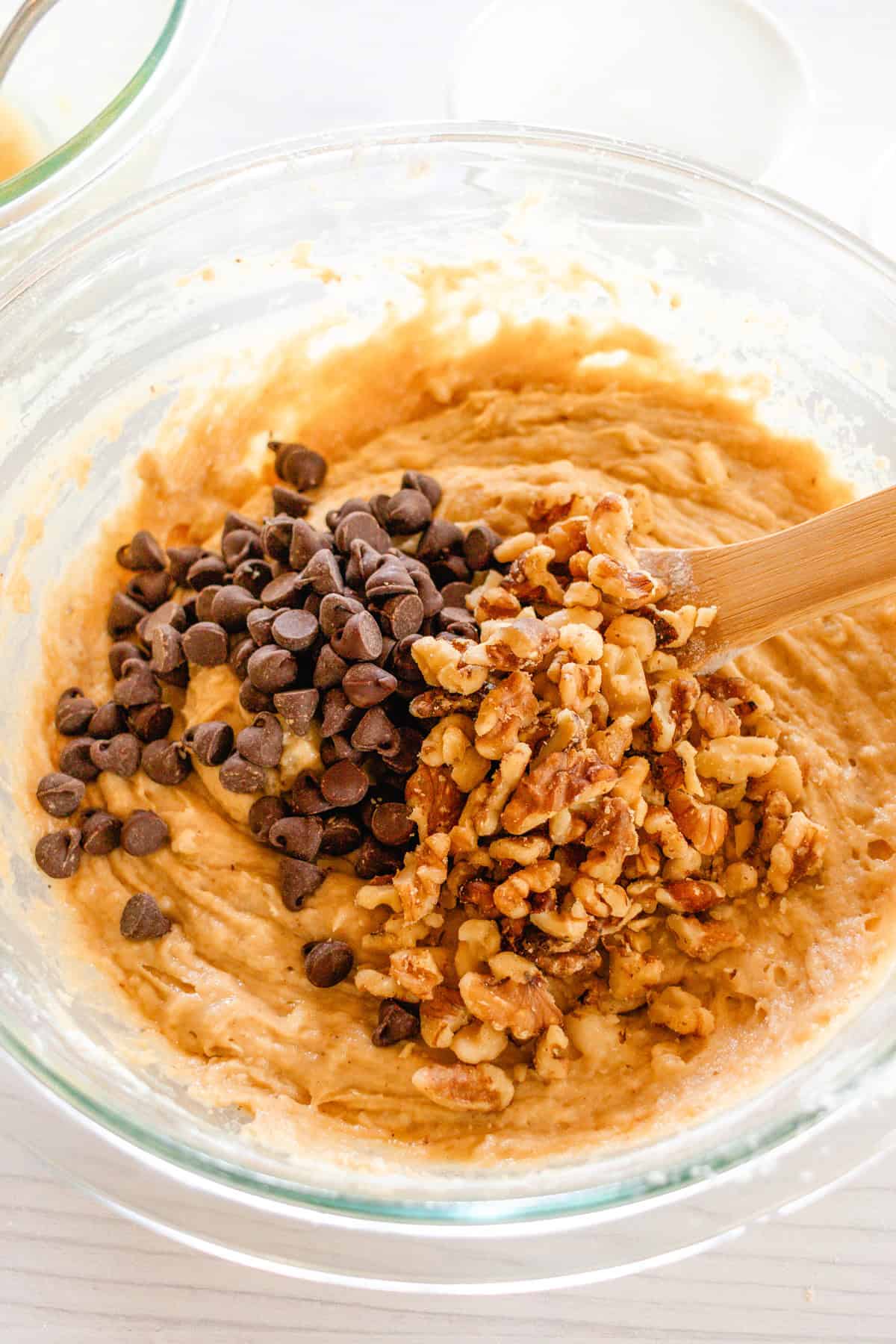 Adding the chocolate chips and walnuts to the batter and folding in with a wooden spatula. 
