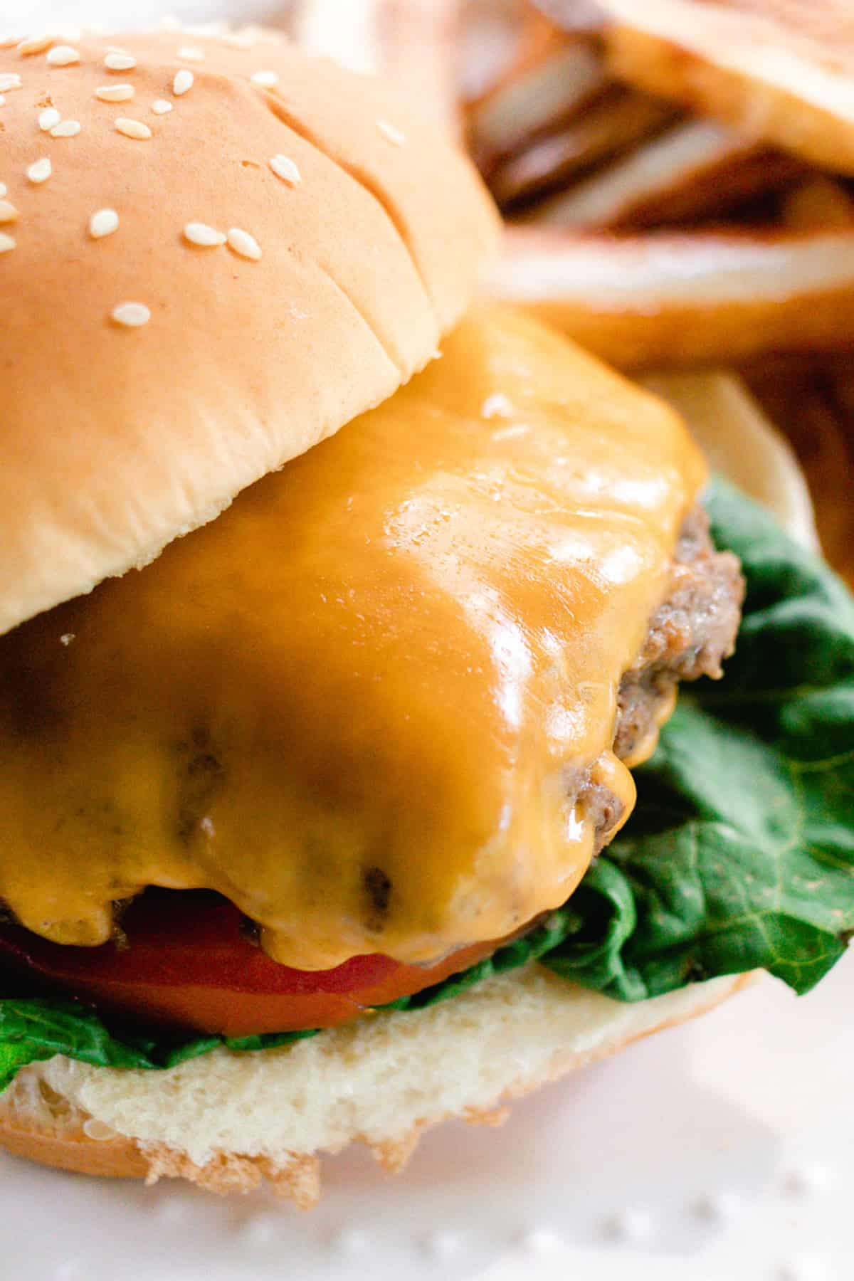 Topping the burger with cheese and dressing it up with a bun, lettuce and tomatoes.