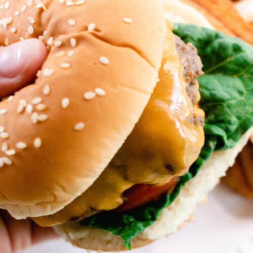 Holding a burger with a sesame seed bun and melted cheese.