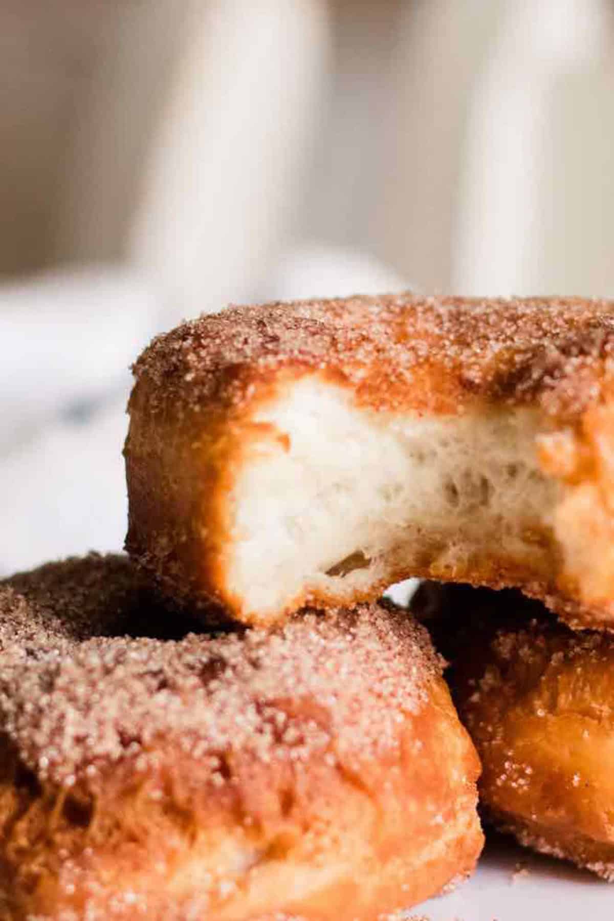 Three freshly made donuts stacked with the top one having a bite taken out.