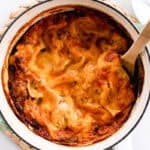 Dutch oven lasagna in a large dutch oven on a hot pad with a wooden spoon in it.