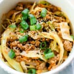 Egg roll bowl, topped with green onions and sesame seeds on a wooden table.