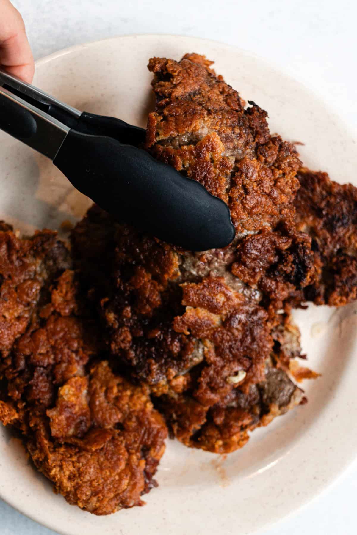 Setting a piece of fried beef liver on a plate with a pair of tongs.