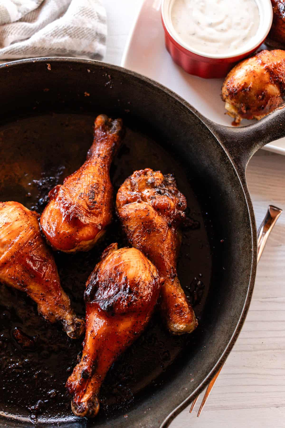Cast iron chicken drumsticks in a large cast iron skillet with a small bowl of ranch next to it.
