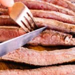 Slicing flank steak with a sharp knife on a wooden cutting board.