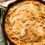 Cast iron quiche on a white wooden table with a blue towel next to it.