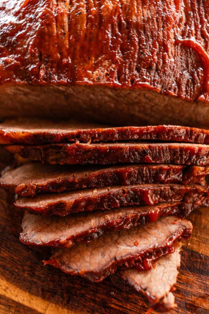 Cutting a dutch oven brisket with the slices falling off of the wooden cutting board.