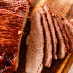 Tender beef brisket with caramelized barbecue sauce and a few slices cut out of it on a wooden cutting board.