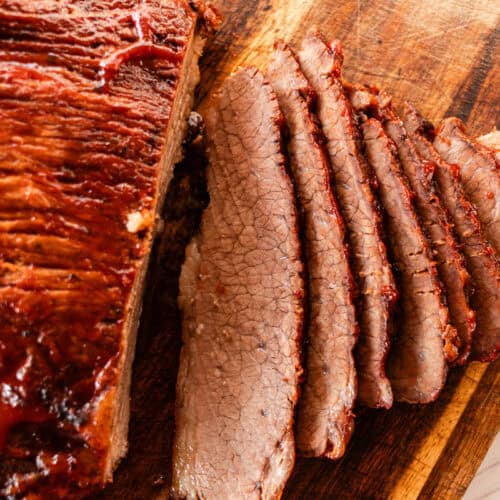 Tender beef brisket with caramelized barbecue sauce and a few slices cut out of it on a wooden cutting board.
