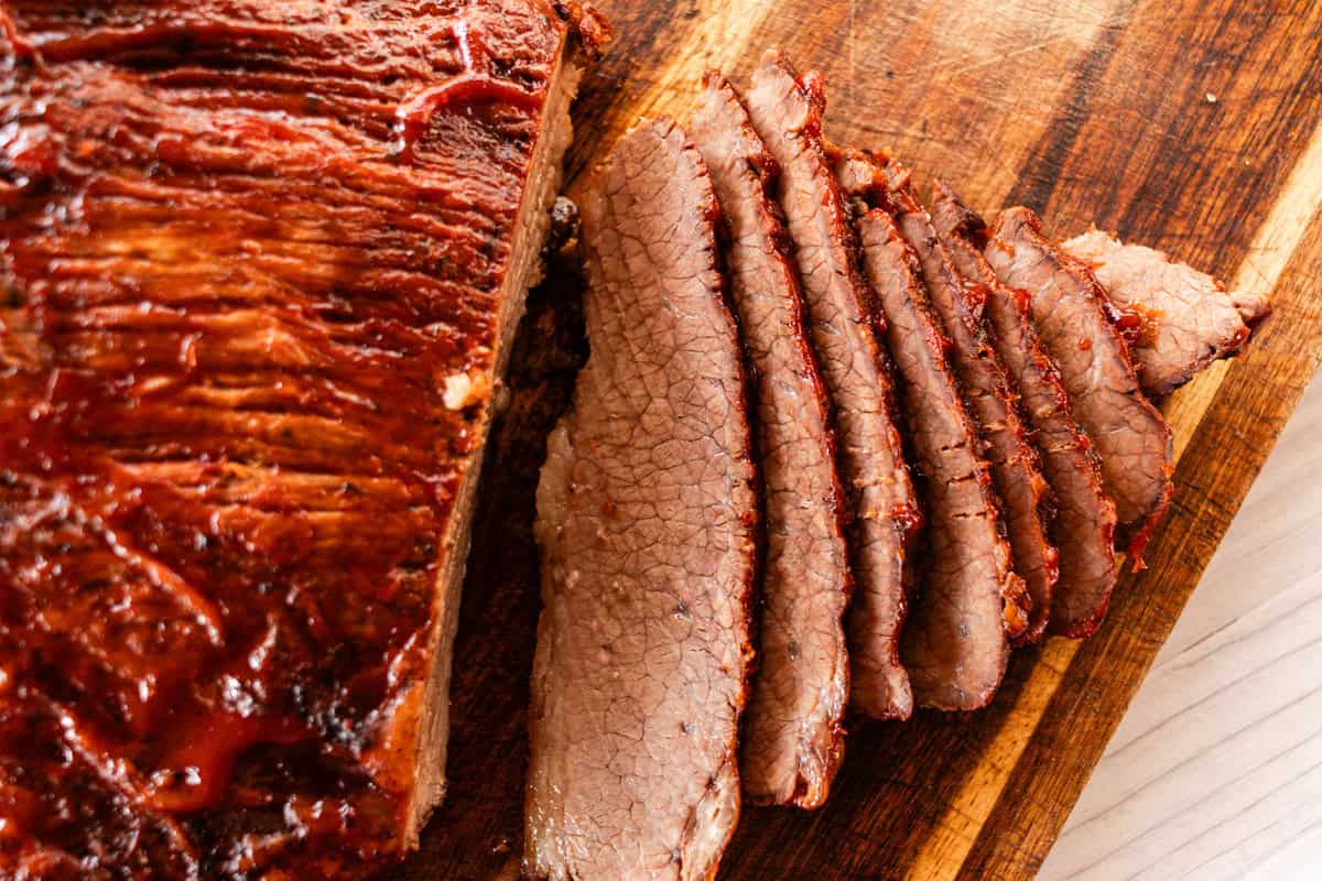 Tender beef brisket with caramelized barbecue sauce and a few slices cut out of it on a wooden cutting board. 