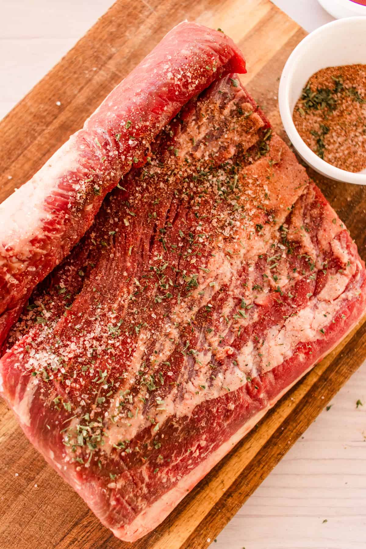 Large brisket with dry rub seasonings pressed into it on a wooden cutting board. 