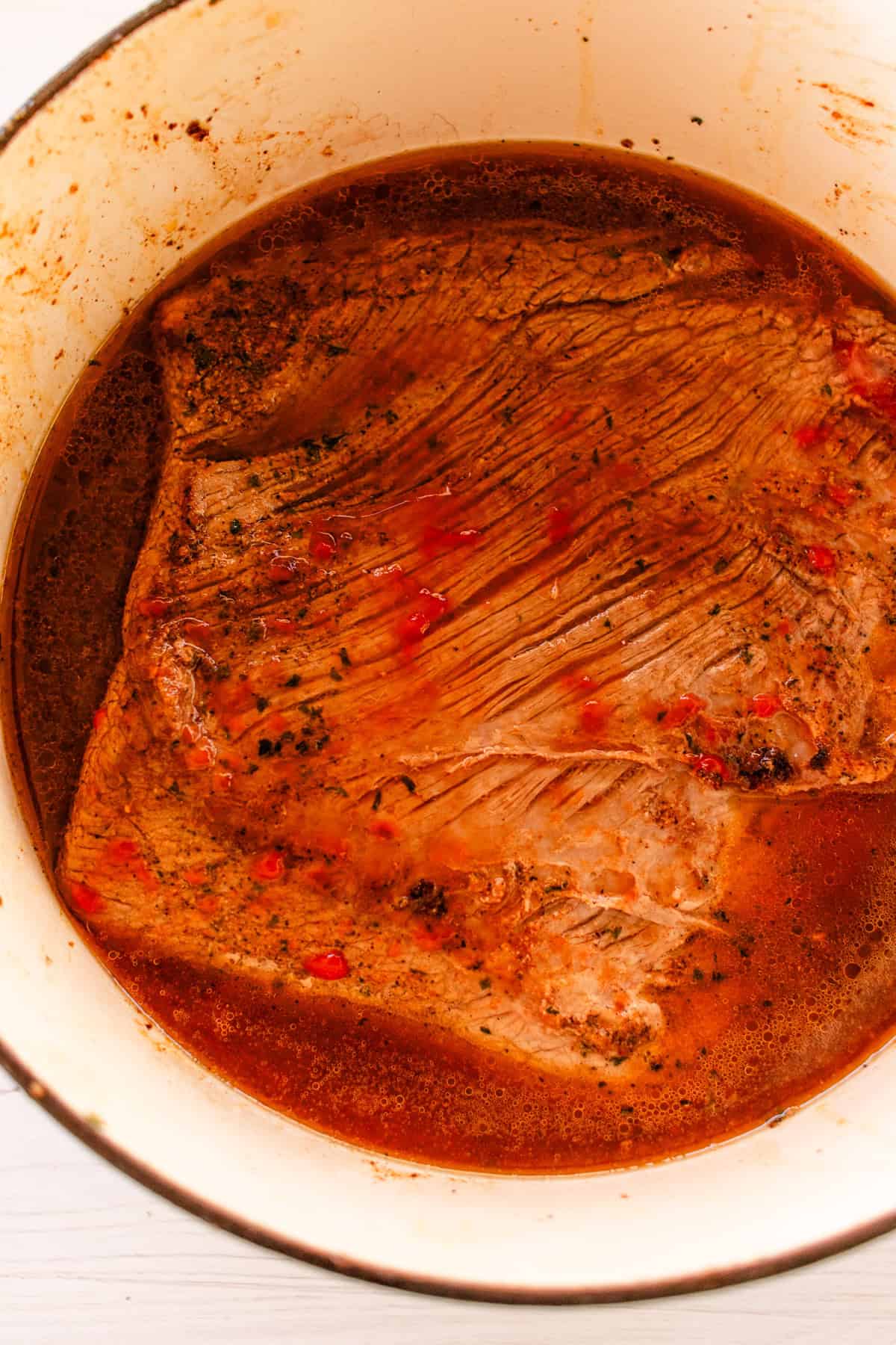 Brisket in the bottom of a dutch oven with the broth all around it.