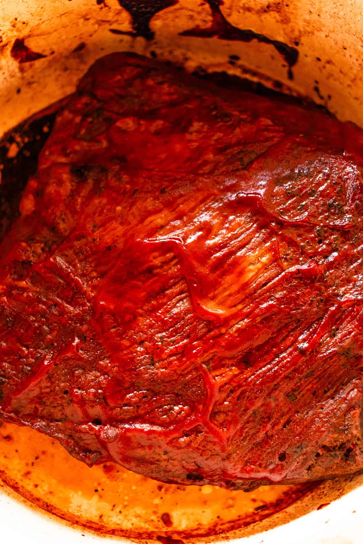 The brisket in the dutch oven with barbecue sauce on top.