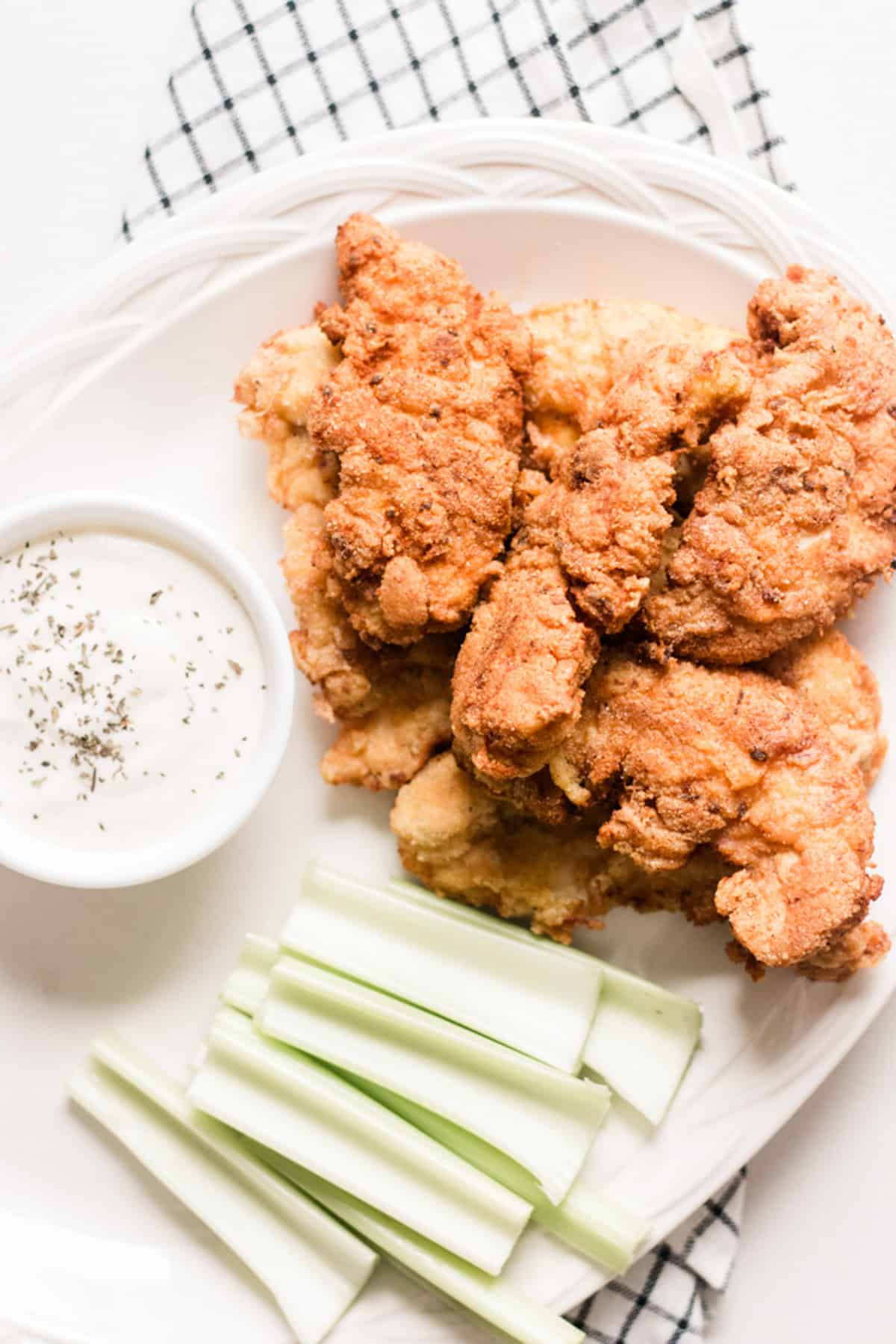 Dutch oven fried chicken piled high on a white serving plate with celery and homemade ranch.