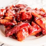 Sticky pork belly burnt ends piled high on a white plate with a checkered tea towel next to it.