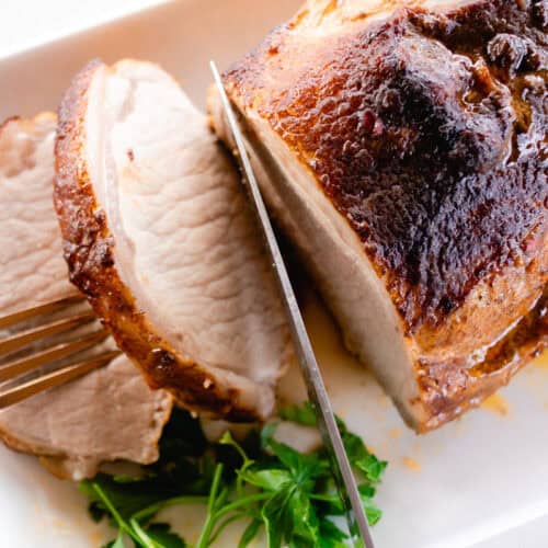 Pork loin roast cut in slices on a platter with gravy and a glaze on top.