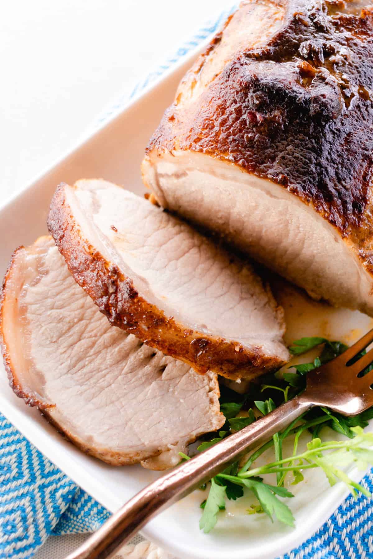 Slices of pork loin roast on a white serving tray with a blue towel next to it. 