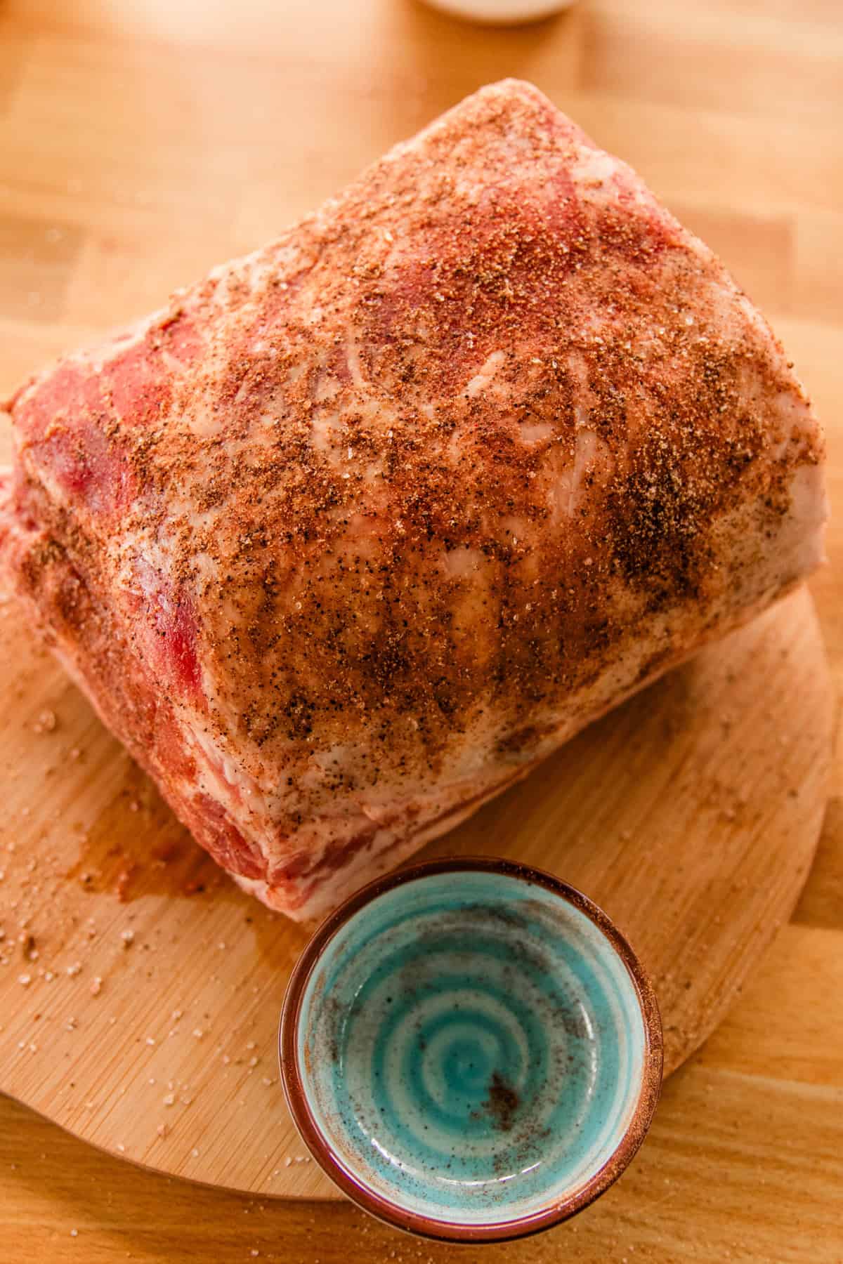 A large pork loin roast covered in a homemade dry rub on a wooden cutting board. 