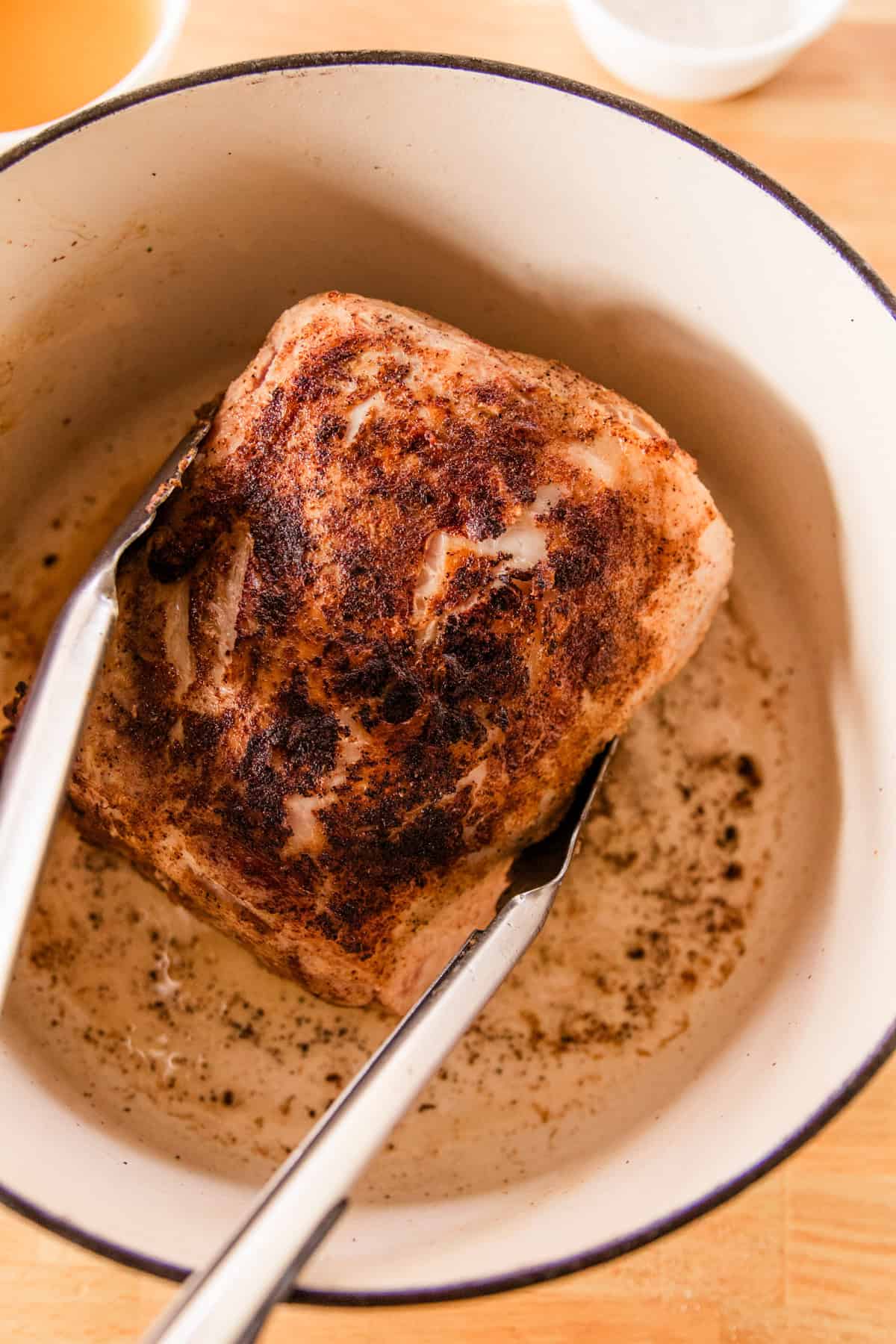 Searing the roast in a dutch oven and flipping it with a pair of tongs. 