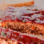 A elk meatloaf with a tangy glaze on top with slices of bread in the background.