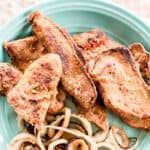 Fried liver with fried onions on a green plate.