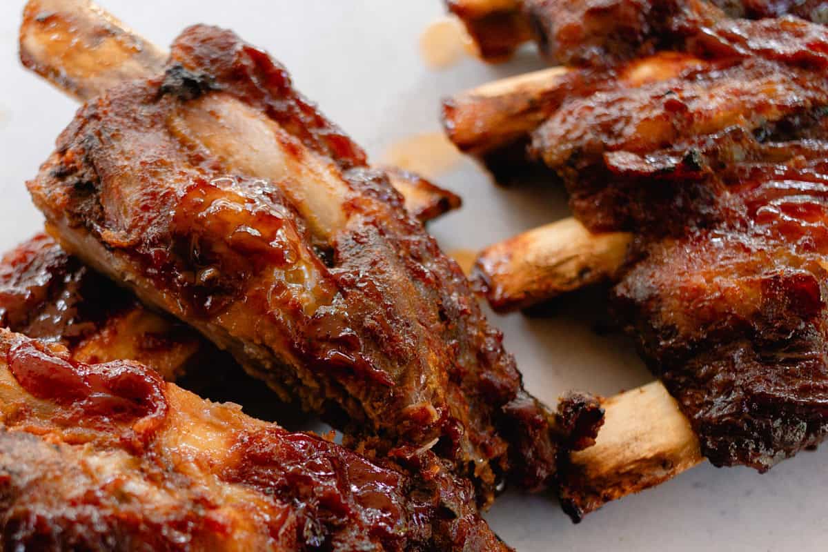 Oven baked beef ribs stacked on a white table top.