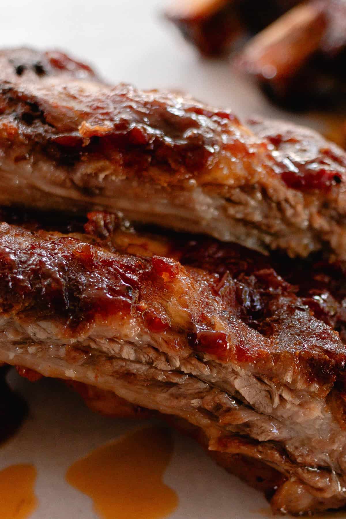 2 beef ribs on a white plate dripping in bbq sauce. 