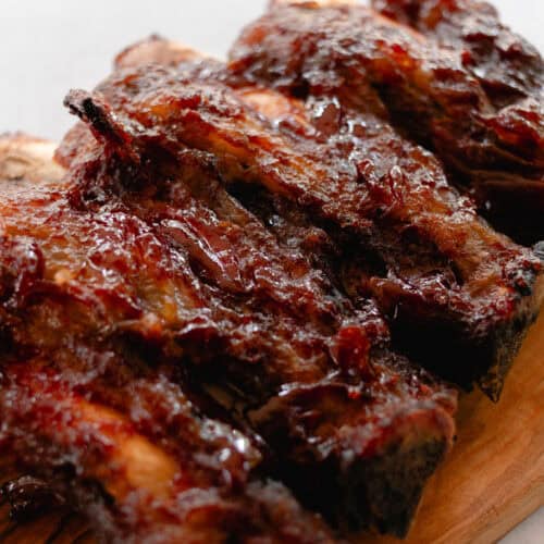 A small rack of beef back ribs cooling on a wooden cutting board.