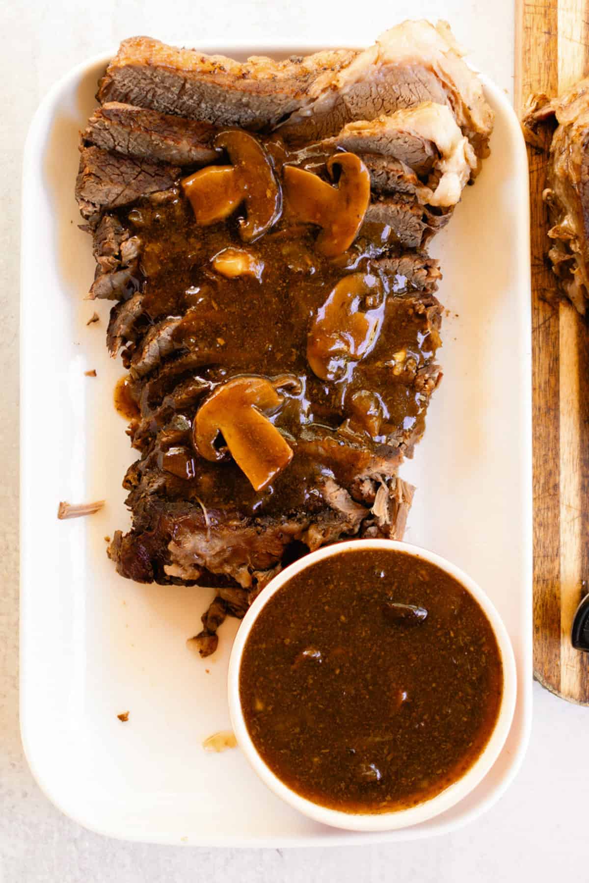Coffee gravy covering a heel of round roast with a bowl of extra gravy on a plate.
