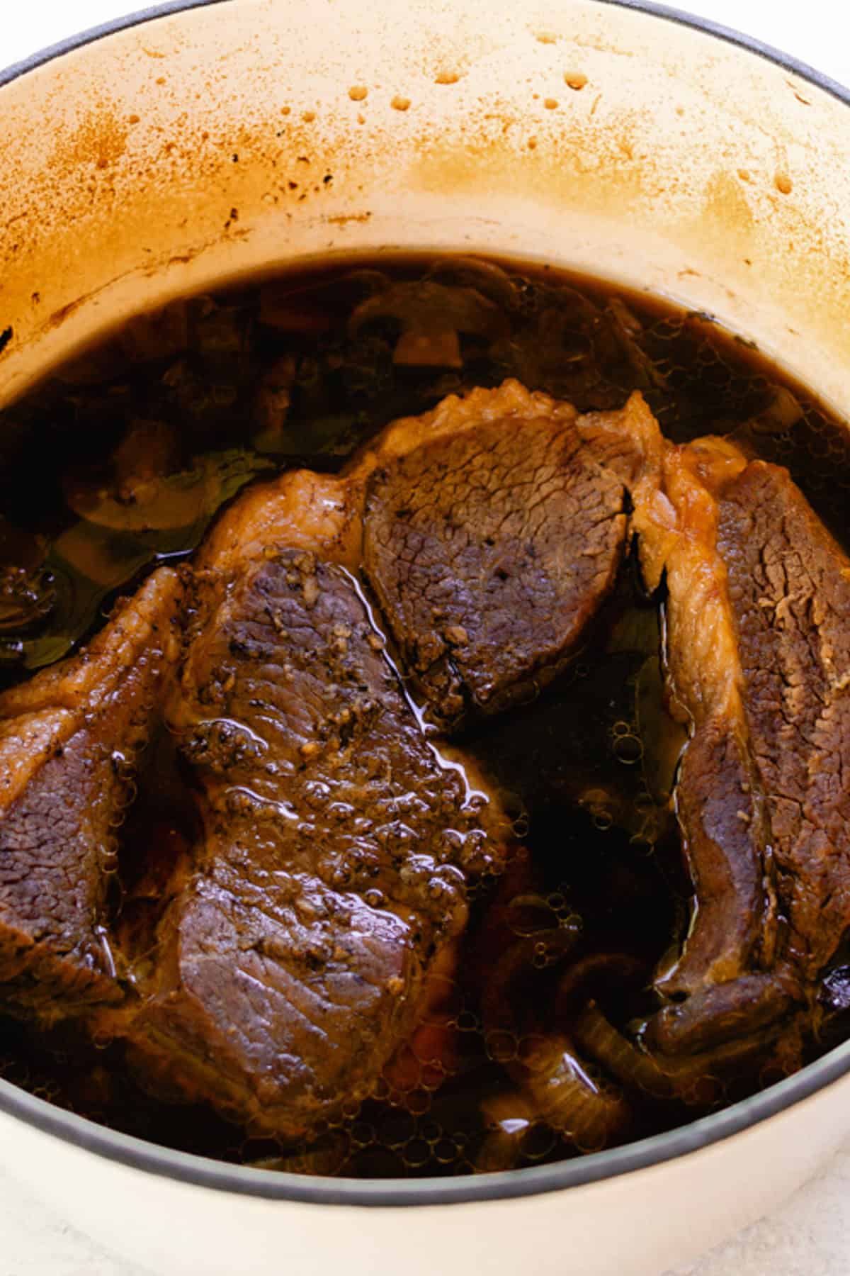 Cooked pikes peak roast with the broth and vegetables surrounding it. 